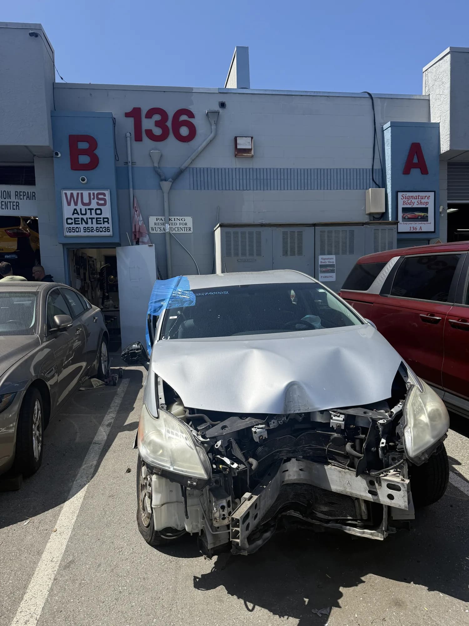 Vehicle with severe front-end collision damage outside the Wu's Auto Center repair bays